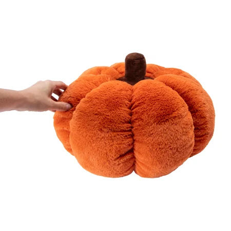 Side view of the orange Halloween pumpkin pillow with a hand shown beside its rounded design sold by LFG Energy Club.
